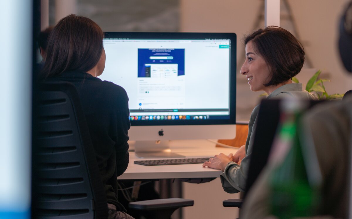 Zwei Kolleginnen von Homepage Helden besprechen ein Website-Projekt am iMac.