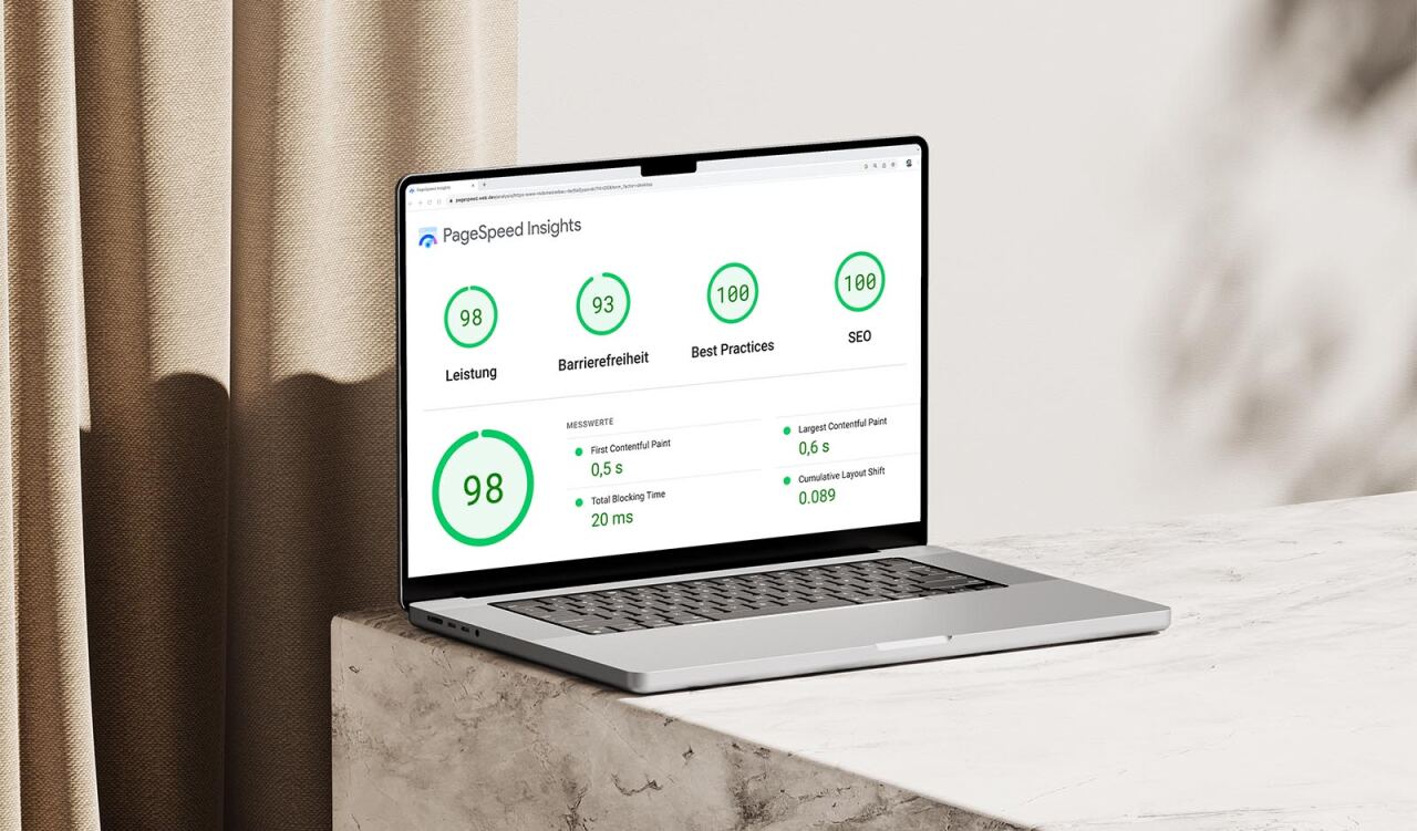 Laptop zeigt PageSpeed Insights mit folgenden Werten: PageSpeed Insights; 98 Leistung; 93 Barrierefreiheit; 100 Best Practices; 100 SEO; 98; MESSWERTE: First Contentful Paint 0,5 s; Total Blocking Time 20 ms; Largest Contentful Paint 0,6 s; Cumulative Layout Shift 0.089. Laptop steht auf Marmorplatte vor beigefarbenem Vorhang und hellem Hintergrund.