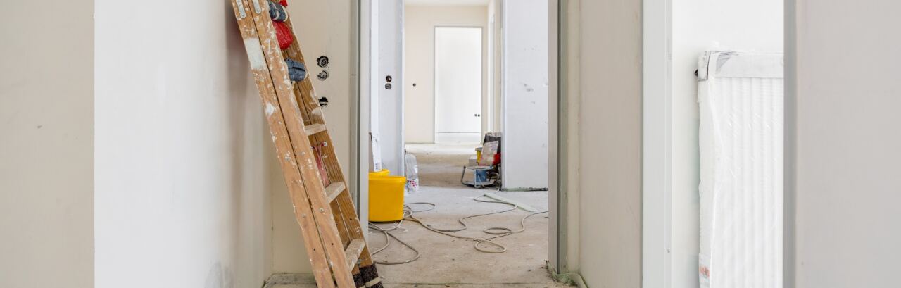 Wohnung im Innenausbau: Leiter an der frisch verputzten Wand, Kabel und Eimer auf dem Estrich, Blick in die nächsten Räume.