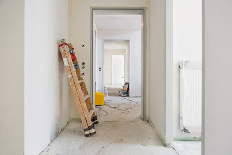 Wohnung im Innenausbau: Leiter an der frisch verputzten Wand, Kabel und Eimer auf dem Estrich, Blick in die nächsten Räume.