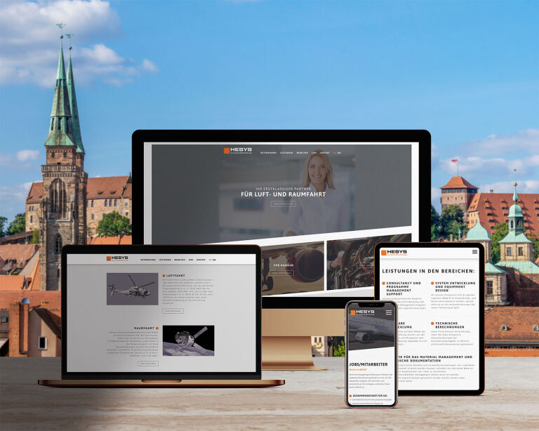 Mehrere Bildschirme (Desktop, Laptop, Tablet, Smartphone) zeigen eine Unternehmenswebsite. Sichtbarer Text: HESYS; FÜR LUFT- UND RAUMFAHRT; LEISTUNGEN IN DEN BEREICHEN:; LUFTFAHRT; RAUMFAHRT; JOBS/MITARBEITER. Im Hintergrund Stadtsilhouette mit Kirchturm.